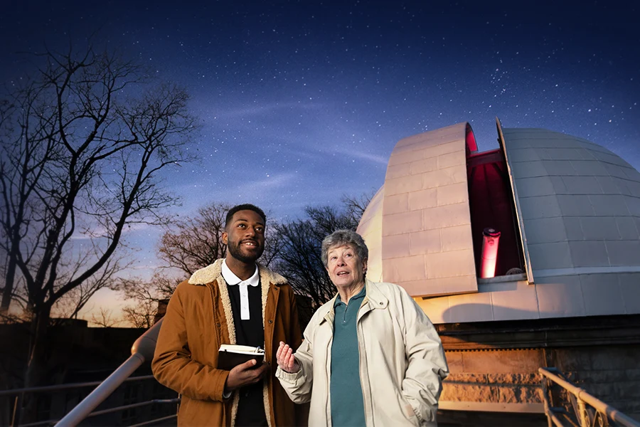 A male student gazes into the starry sky at the campus observatory as his instructor points out something in the sky.